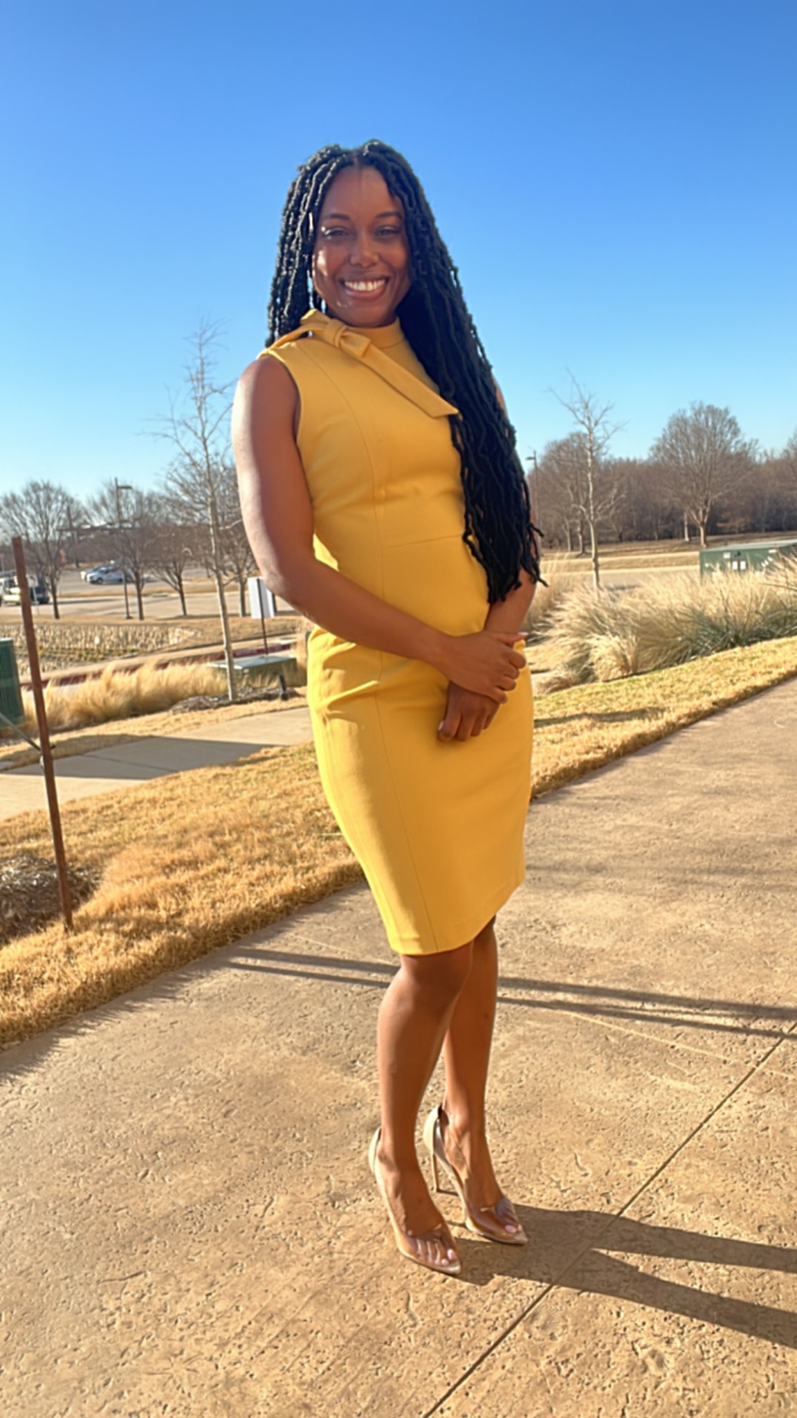 Francine smiling outdoors in a yellow dress.